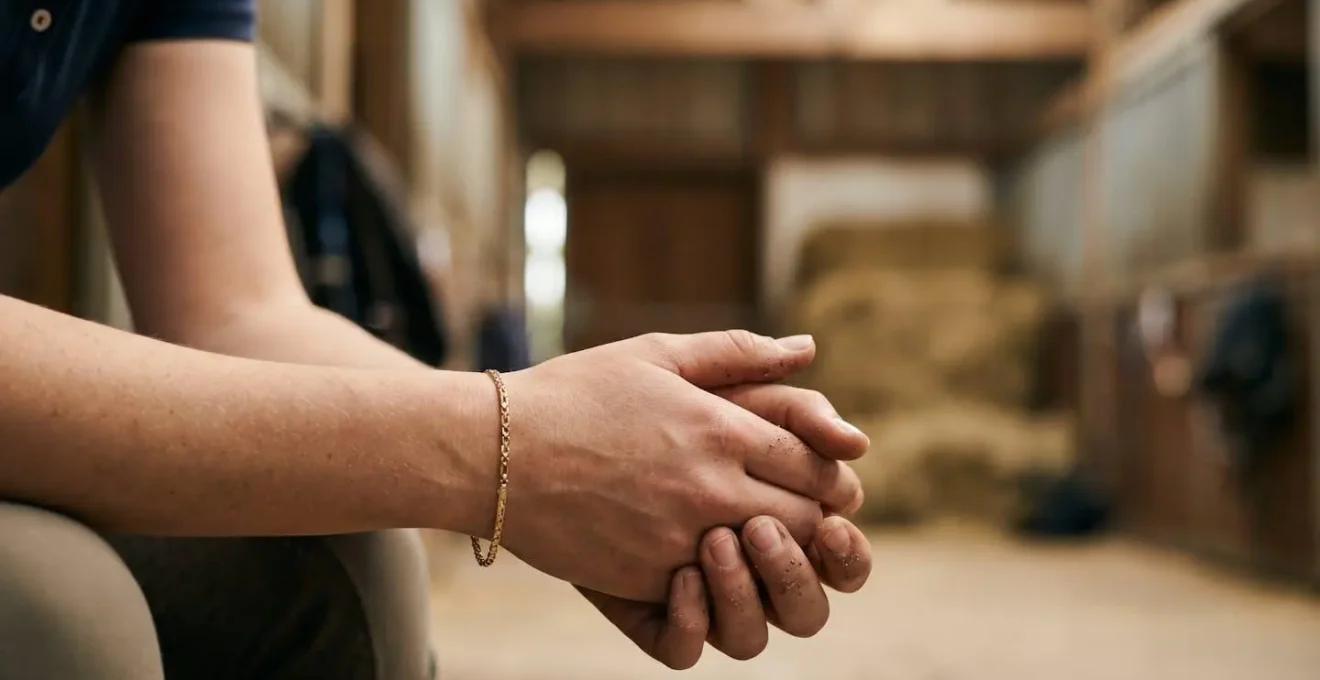 Mains d'un cavalier manipulant délicatement une bague fine dans l'environnement d'une écurie