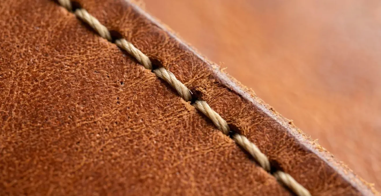 Gros plan sur une couture sellier artisanale montrant l'inclinaison caractéristique du fil sur du cuir de qualité