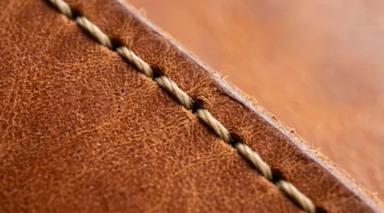 Gros plan sur une couture sellier artisanale montrant l'inclinaison caractéristique du fil sur du cuir de qualité