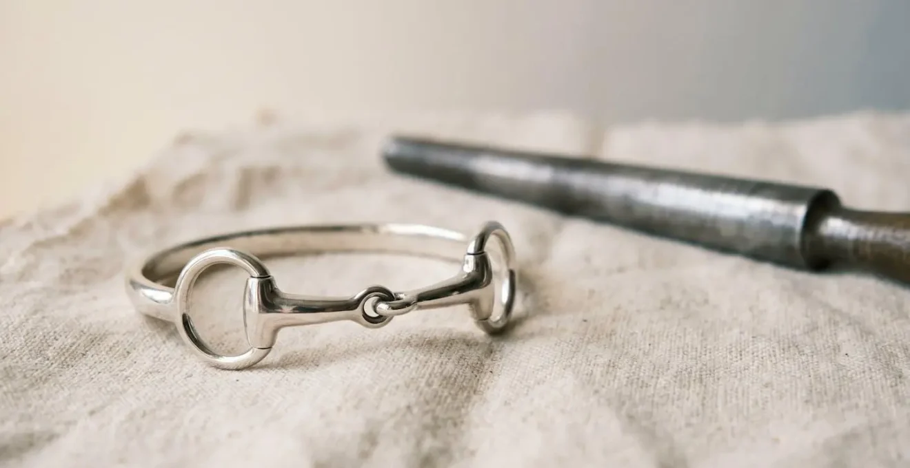 Gros plan sur un jonc mors équestre en argent reposant sur un support neutre avec un outil d'ajustement professionnel à côté