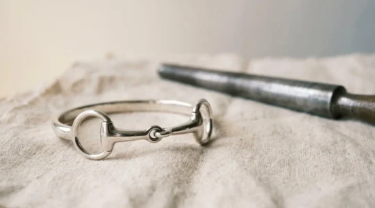 Gros plan sur un jonc mors équestre en argent reposant sur un support neutre avec un outil d'ajustement professionnel à côté