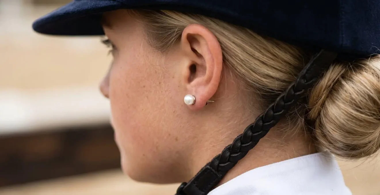 Gros plan sur des puces d'oreilles discrètes portées par une cavalière en tenue de concours